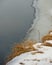 Dry grass in the snow against the background of melting ice in the river. Natural background