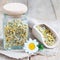 Dry herbal chamomile tea in jar and wooden scoop with fresh chamomile flowers on background, square format