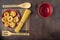 Dry macaroni in a red ceramic dish on a background of bamboo appliances and a walnut-colored wooden table top