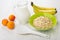 Dry oat flakes, milk, bananas, apricots, white spoon on table