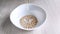 Dry oatmeal is poured into empty white bowl. Cooking healthy nutritious breakfast. Close-up, daylight