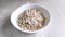 Dry oatmeal is poured into white bowl. Cooking healthy nutritious breakfast. Close-up, daylight