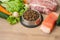 Dry pet dog food with natural ingredients. Raw meat, fish, vegetables, eggs and salad near bowl with dry pet feed on wooden