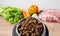 Dry pet dog food with natural ingredients. Raw meat, vegetables, eggs and salad near bowl with dry pet feed on wooden background.