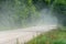 A dry sandy road passes through a field under the scorching sun and clouds. Dirt road outside the city along the forest. Dust