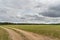 A dry sandy road passes through a field under the scorching sun and clouds. Dirt road outside the city in the village. Arid