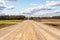 A dry sandy road passes through a field under the scorching sun and clouds. Dirt road outside the city in the village. Arid