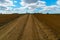 A dry sandy road passes through a field under the scorching sun and clouds. Dirt road outside the city in the village. Arid