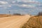 A dry sandy road passes through a field under the scorching sun and clouds. Dirt road outside the city in the village. Arid
