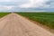 A dry sandy road passes through a field under the scorching sun and clouds. Dirt road outside the city in the village. Arid