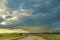 A dry sandy road passes through a field under the scorching sun and clouds. Dirt road outside the city in the village. Arid