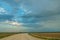 A dry sandy road passes through a field under the scorching sun and clouds. Dirt road outside the city in the village. Arid