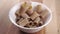 Dry uncooked brown integral rigatoni pasta fill a white kitchen bowl on a wooden surface.