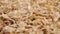 Dry uncooked cereal spelt flakes fall on a pile.