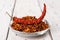Dry wrinkled pod of red hot pepper on a heap of pepper flakes in a glass saucer on a rustic wood table. Natural spices and