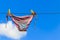 Drying female swimsuit hanging on rope against blue sky