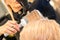 Drying straight blond hair with black hairdryer and white round brush in hairdresser salon, close up.