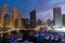 Dubai marina with boats and buildings with gates at night with lights and blue sky