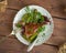 Duck baked leg with greens and cherry jam on a ceramic round plate, served on a wooden tray with Cutlery