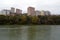 Dull and bleak view of old multi-storey houses, glum sky, autumn forest and the lake