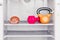 Dumbbell, kettlebell and a sandwich on the shelf of the refrigerator. The choice between a healthy lifestyle and unhealthy diet