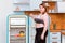Dumbbell and kettlebell on the shelf of the refrigerator. Fat woman stands next to the fridge choosing a sport
