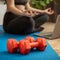 Dumbbells and unrecognizable sporty woman making meditation yoga fitness stretching at home via laptop. Young woman losing weight