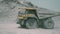 A dump truck drives in a dusty open pit mine.