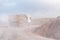 Dump truck entering a quarry to unload gravel, covered in dust