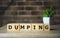 Dumping Word Written In Wooden Cubes on brick background .