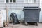 Dumpster on the grey wall background. Garbage bin near housing