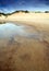 Dunes reflects in water with cloudy sky.