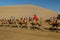 DUNHUANG, CHINA - AUGUST 21, 2018: Tourists ride camels at Singing Sands Dune near Dunhuang, Gansu Province, Chi