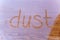 Dust written on dusty wooden surface partly cleaned.