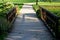 Dusty park path along the pond winding through a meadow. it leads to the bridge and the share of the way are long benches with woo