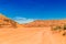 Dusty and unpaved road through the arid and dry desert. Desert with sand dunes and blue sky.