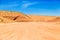 Dusty and unpaved road through the arid and dry desert. Desert with sand dunes and blue sky.