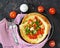 Dutch baby pancake filled tomatoes, sausages and cheese in a serving cast-iron frying pan on a dark concrete background. Danish