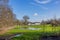 Dutch farmland with a puddle of water on green grass, bare trees with Genhoes castle in the background