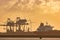 Dutch industrial plant with chimneys and windmill with cargo ship in front during sunset in Europoort, Rotterdam harbor