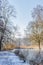 Dutch nature reserve with a footpath with snow, a stream with its frozen waters and bare trees and light mist