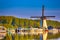 Dutch Windmill In Front of The Canal With Moored Motorboats at Marina Located in Traditional Village in The Netherlands. Shot at