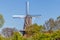 Dutch windmill with its brick tower and blades with white lines, surrounded by lush green trees