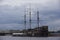 Dutch wooden fluyt merchant sailing ship of XVIII century with three wooden masts on a grey sky and clouds background