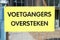 A Dutch yellow sign that says \'Pedestrians please traverse