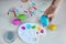 Dyeing easter egg. Women`s hand with paintbrush on background of paints in palette and colorful eggs on table, view from above