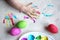 Dyeing easter eggs. Paints in palette, colorful eggs and child palm on table, view from above
