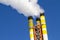 Dynamic angle of chimney from a refuse incinerator emitting smoke and polluting the air against a clear blue sky