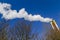 Dynamic angle of chimney from a refuse incinerator emitting smoke and polluting the air against a clear blue sky