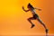 Dynamic image of professional female runner, athlete in motion, running over orange studio background in neon light